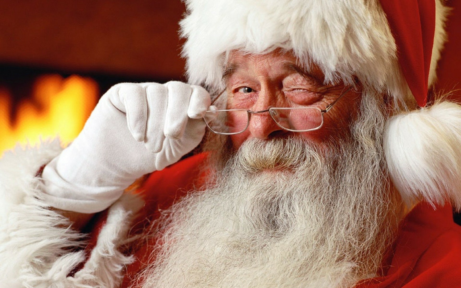 HD holiday wallpaper featuring Santa Claus winking warmly, wearing glasses and a traditional red suit, embodying the festive Christmas spirit.