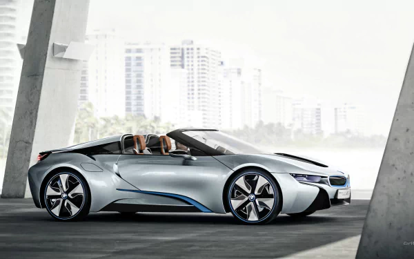 Sleek silver BMW i8 Concept Spyder roadster in profile under a modern overpass, sunlit city skyline in the background — HD PC desktop wallpaper/background.