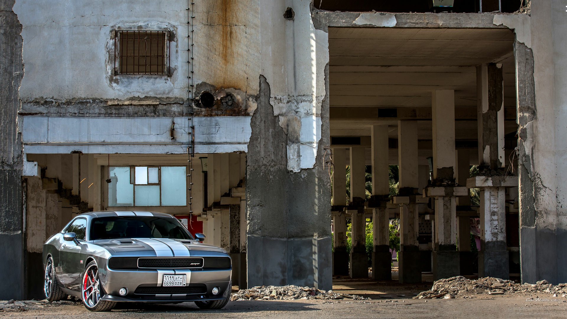 HD PC desktop wallpaper: Dodge Challenger SRT8 muscle vehicle with white racing stripes parked by a weathered industrial building and open concrete pillars.