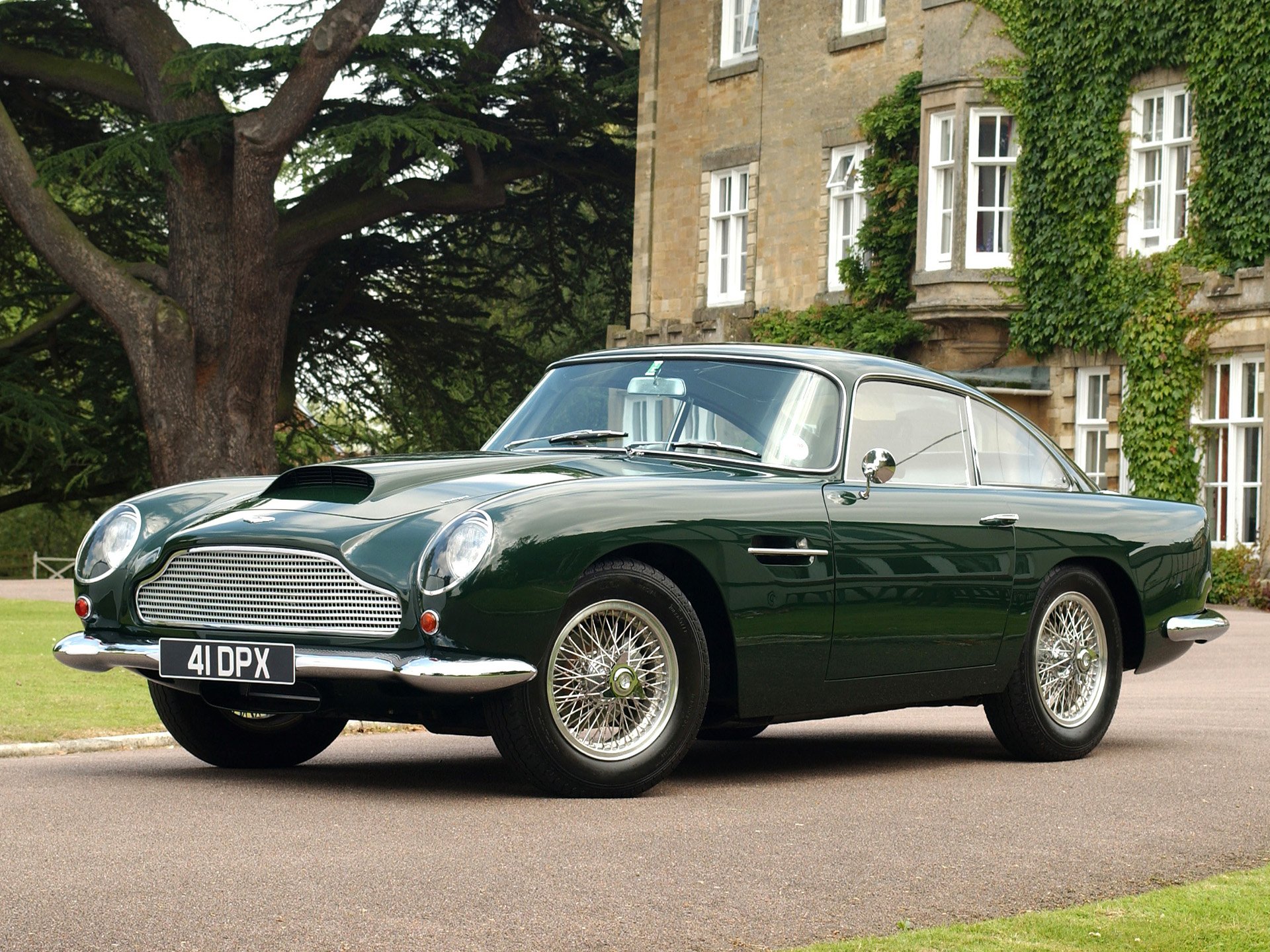 Aston Martin DB4 vehicle in dark green parked in front of a historic building, showcased as an HD PC desktop wallpaper and background.