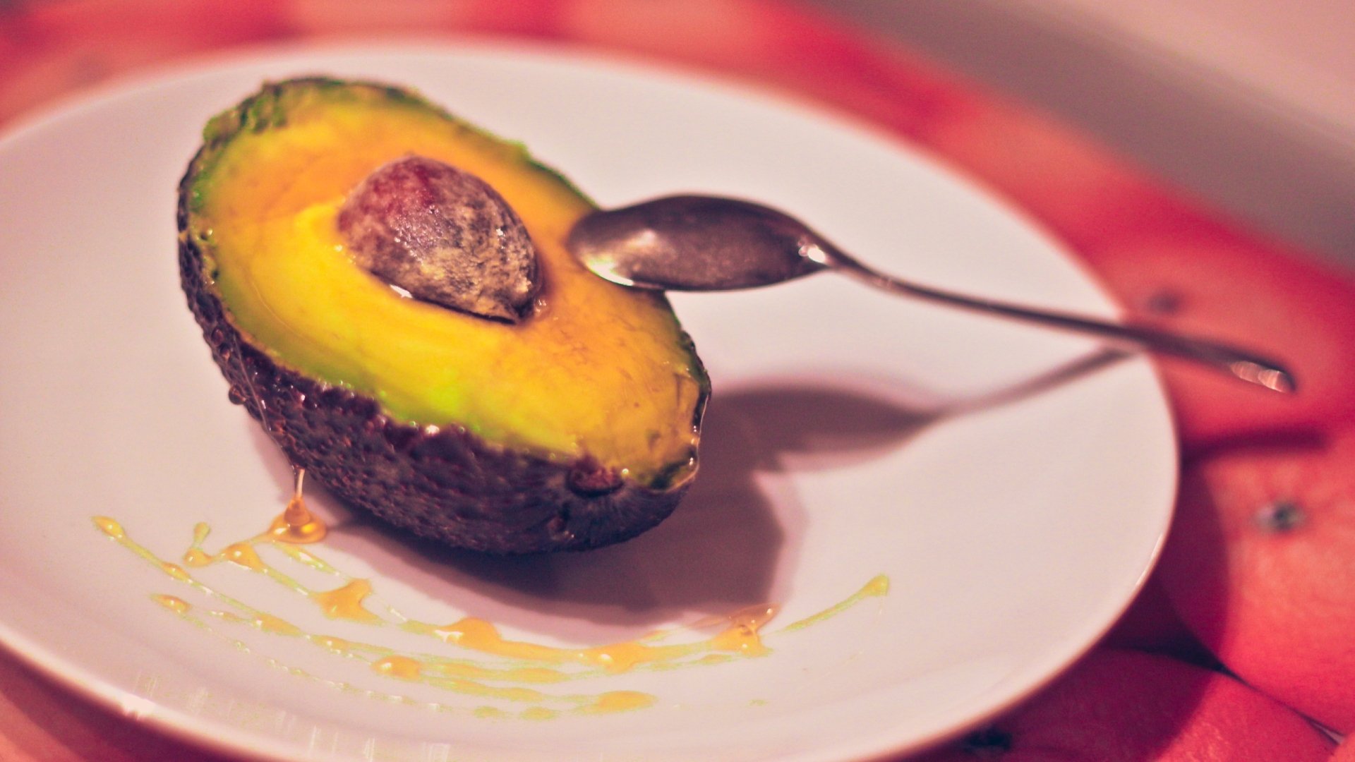 HD desktop wallpaper featuring a close-up of half an avocado with honey drizzled on a white plate, accompanied by a spoon.