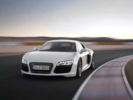HD PC desktop wallpaper featuring a sleek white Audi sports car speeding on a curved racetrack at sunset.