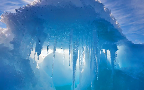 HD desktop wallpaper showcasing a stunning natural ice formation with icicles hanging beneath a translucent blue icy arch against a bright sky.
