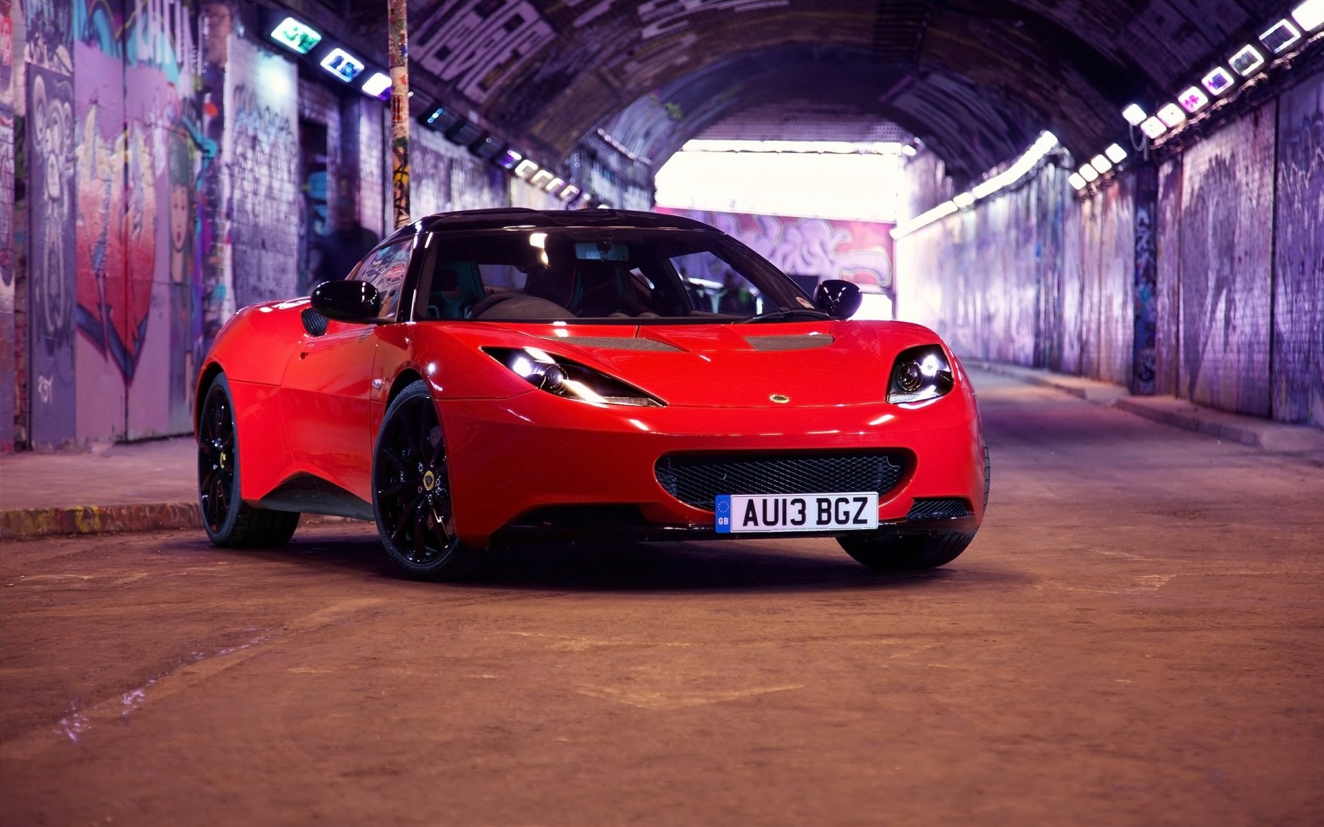 HD desktop wallpaper featuring a red Lotus sports car parked in an urban graffiti-covered tunnel, highlighting sleek design and vibrant colors.