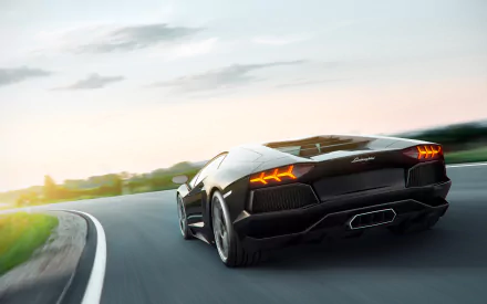 A sleek Lamborghini Aventador speeds down a winding road at sunset, showcasing its dynamic design and powerful presence in this stunning HD desktop wallpaper.