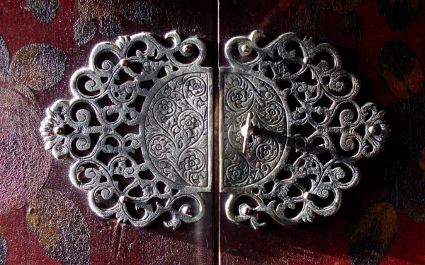 HD PC desktop wallpaper of an ornate man-made metal door fastener with filigree plates and a small key between carved double doors.