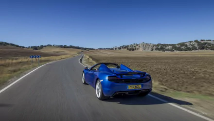 Blue McLaren MP4-12C Spider convertible driving on a winding country road under a clear sky — HD PC desktop wallpaper and background.