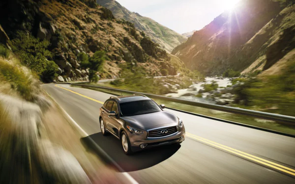 A sleek Infiniti QX70 driving on a winding mountain road, captured in a vibrant HD PC desktop wallpaper with sunlight illuminating the scenic landscape.