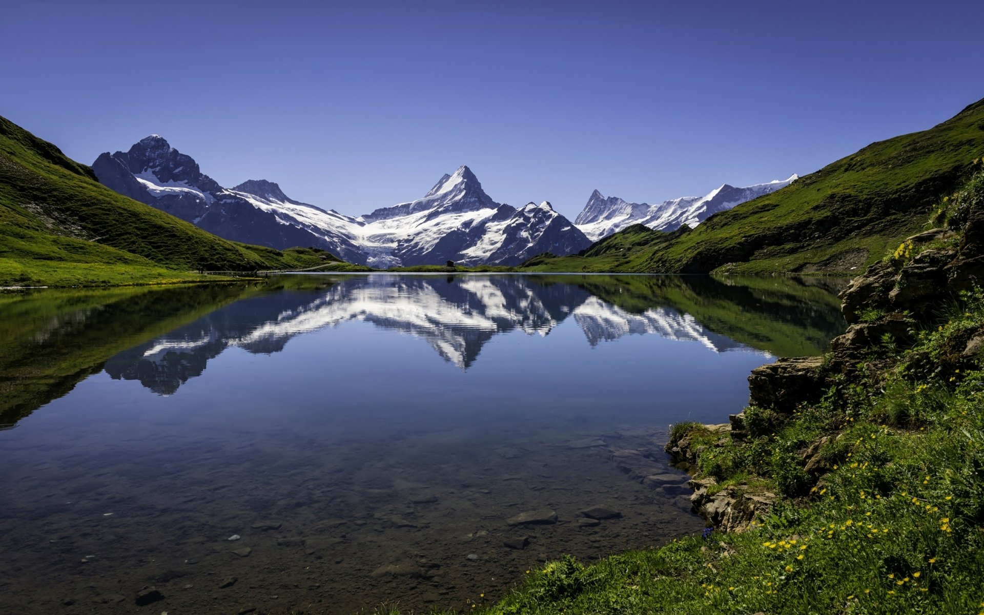 2K Quad HD PC desktop wallpaper background — alpine lake reflecting snow-capped peaks and green slopes under a clear blue sky (nature, reflection).