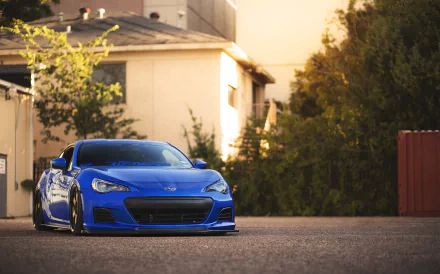 A vibrant blue Subaru BRZ parked in an urban setting, showcasing its sleek design against a backdrop of greenery and buildings. 4K Ultra HD PC desktop wallpaper.