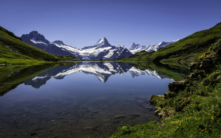 2K Quad HD PC desktop wallpaper background — alpine lake reflecting snow-capped peaks and green slopes under a clear blue sky (nature, reflection).