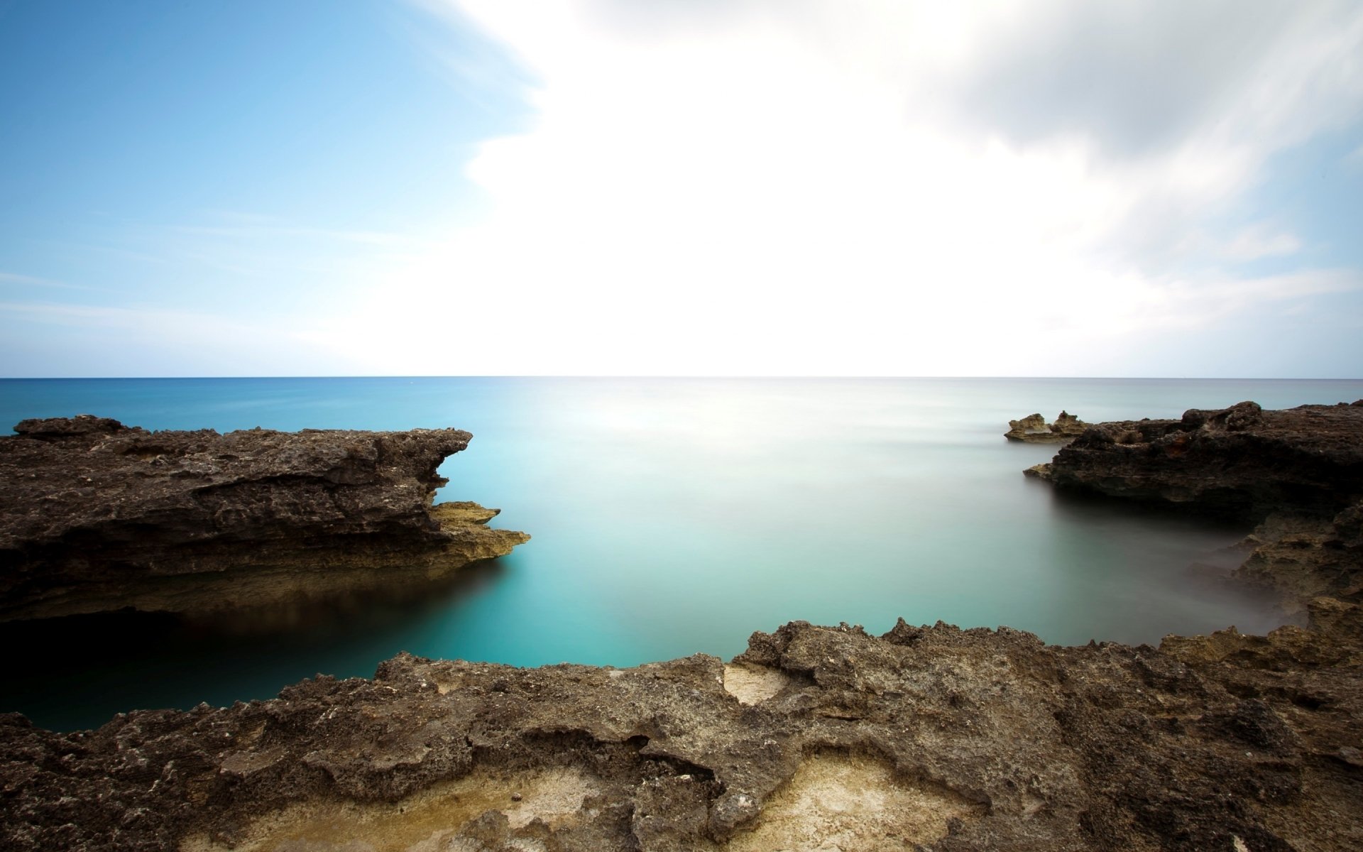 Nature seascape 2K Quad HD PC desktop wallpaper and background: tranquil turquoise sea between rocky ledges under a bright, cloud-diffused sky.