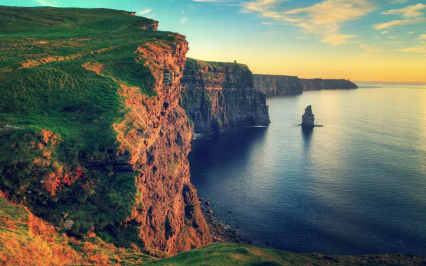 HD desktop wallpaper showcasing a stunning nature scene of towering cliffs beside a calm sea under a vibrant sky during sunset.