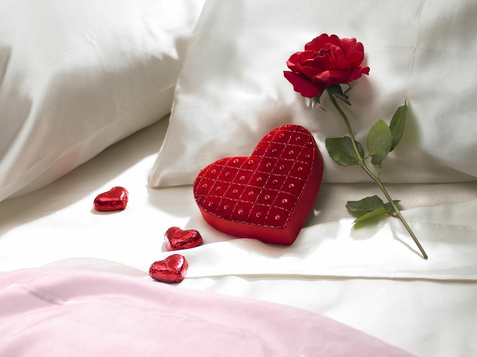HD desktop wallpaper featuring an artistic display of a red heart-shaped pillow, a rose, and small heart accents on a white bedsheet, symbolizing love.
