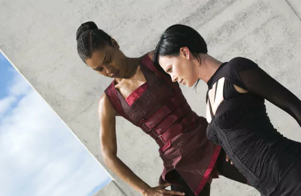 HD PC desktop wallpaper and background: Aeon Flux movie scene showing two women in sleek dark outfits leaning near a concrete wall with blue sky at the edge.