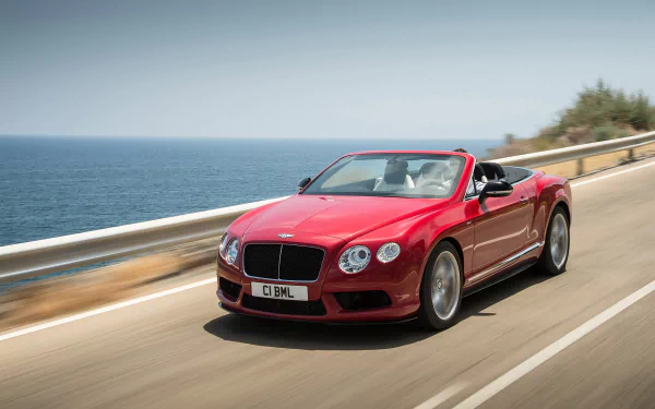 Red Bentley Continental GT V8 convertible cruising on a coastal highway, captured in high-definition for a PC desktop wallpaper background.