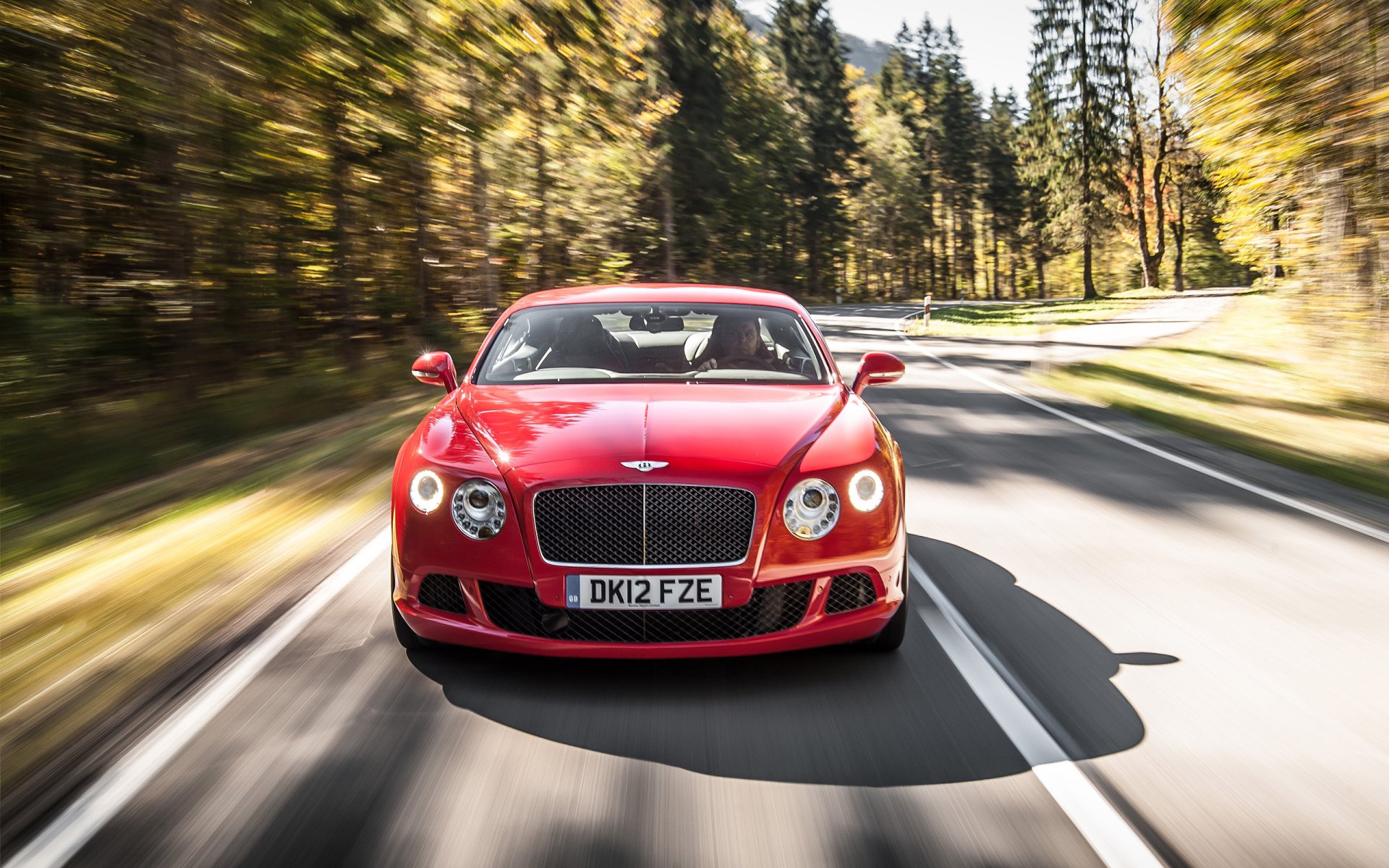 Red Bentley Continental GT Speed speeding down a forest-lined road, captured in sharp HD detail for a dynamic PC desktop wallpaper background.