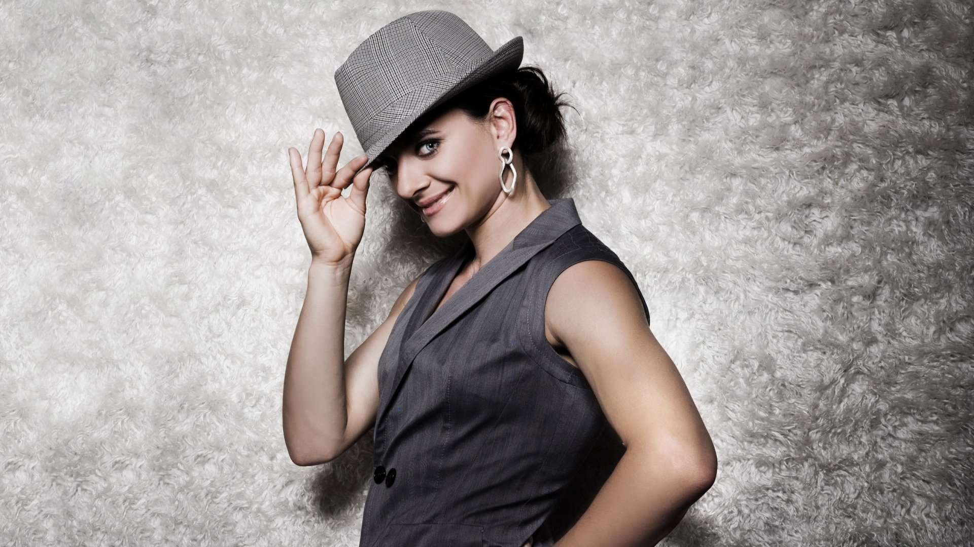 Smiling female athlete in a stylish hat and vest poses against a textured gray backdrop — 2K Quad HD PC desktop sports wallpaper.