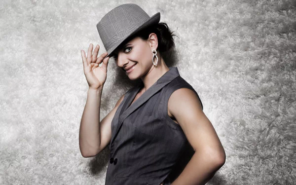Smiling female athlete in a stylish hat and vest poses against a textured gray backdrop — 2K Quad HD PC desktop sports wallpaper.