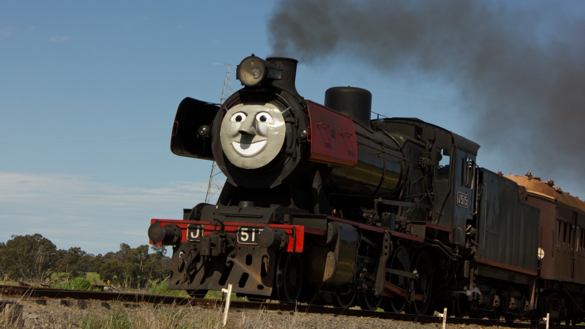 HD PC desktop wallpaper of a steam train locomotive with a cheerful face, billowing smoke and carriages rolling along rural tracks under a clear blue sky.