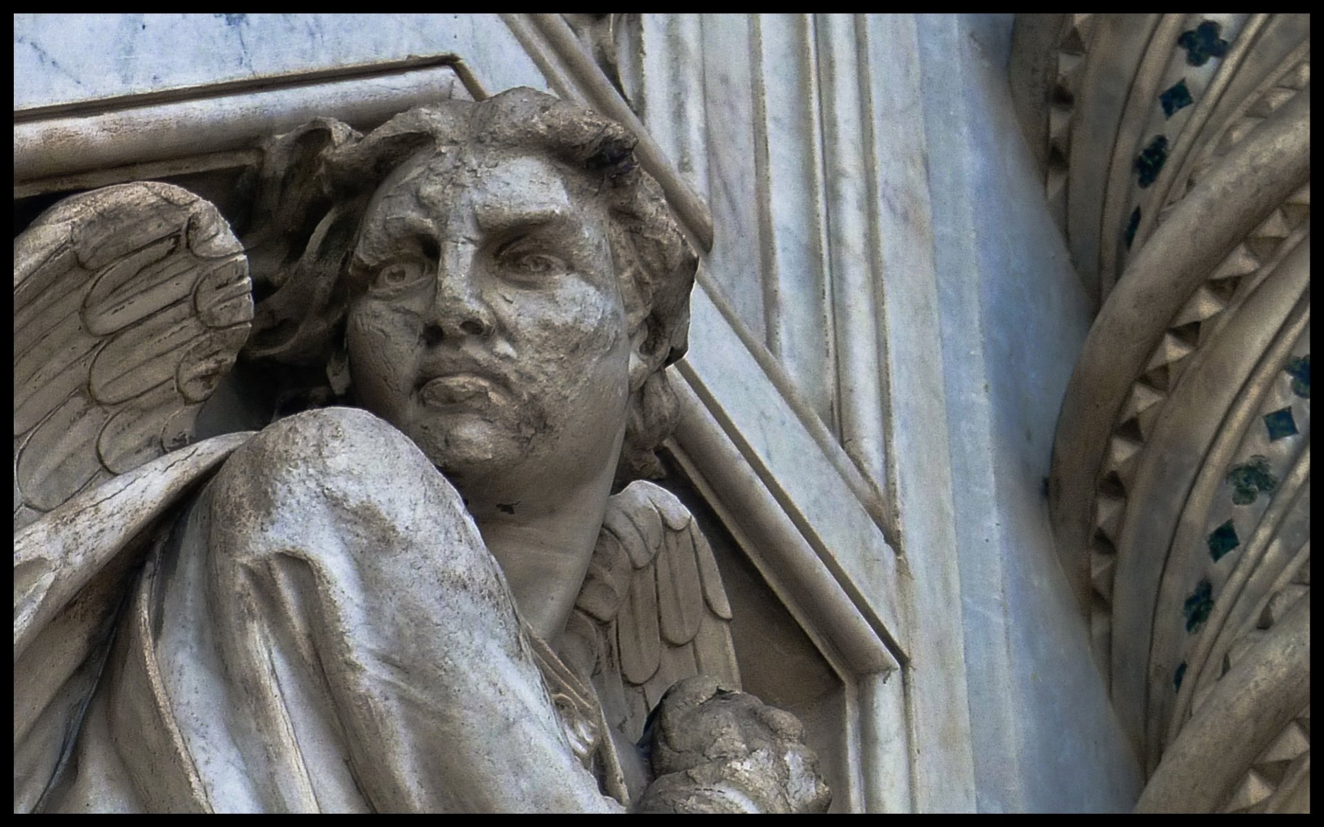 HD PC desktop wallpaper: close-up of a weathered angel statue with carved wings on the facade of the Basilica of Saint Mary of the Flower, religious stone detail.