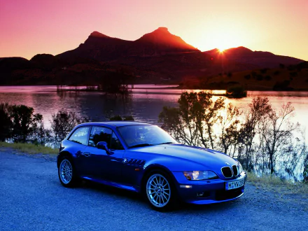 A sleek blue BMW Z3 Coupe parked by a lake at sunset, with mountains in the background, shown as an HD PC desktop wallpaper and background.