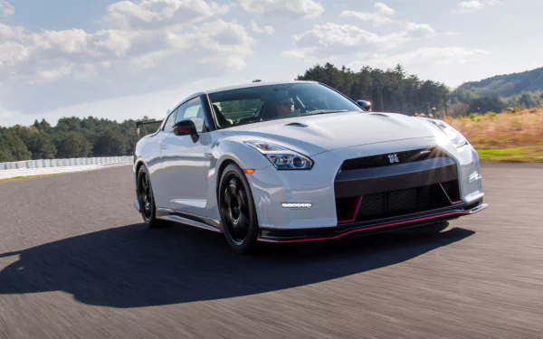 HD PC desktop wallpaper of a white Nissan GT‑R Nismo vehicle on a sunlit racetrack, front three-quarter view with hills and sky in the background.