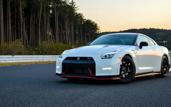 HD PC desktop wallpaper featuring a white Nissan GT-R Nismo parked on a racetrack with trees and a sunset sky in the background.