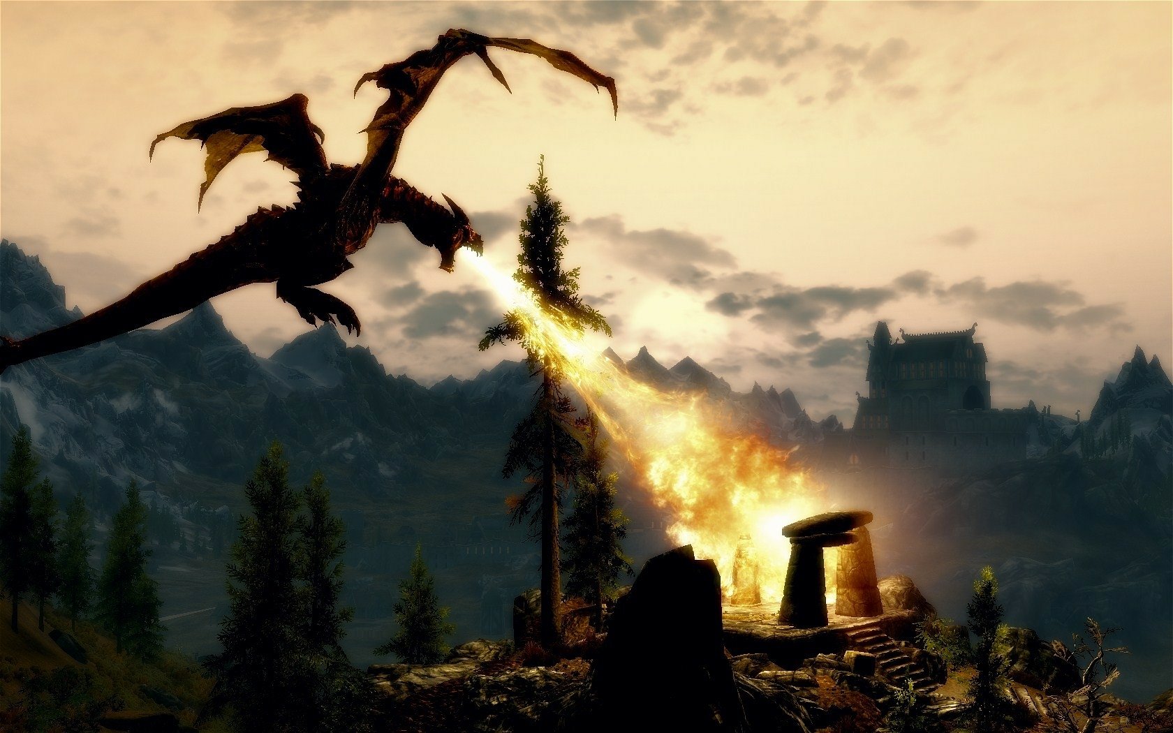A majestic dragon breathes fire in a dramatic landscape from The Elder Scrolls V: Skyrim, featuring mountains and a mystical stone structure against a vibrant sky. HD desktop wallpaper.