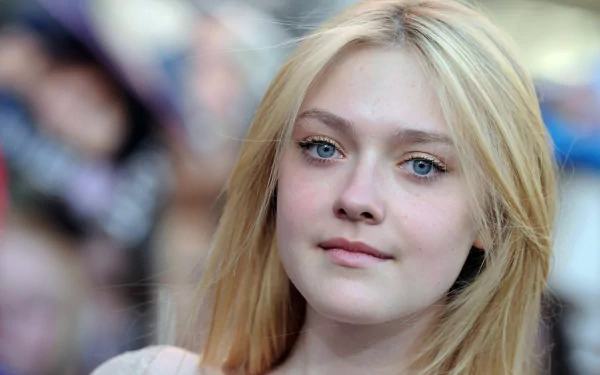 A close-up of Dakota Fanning, an American actress and celebrity, showcasing her striking features and blonde hair against a blurred crowd background.