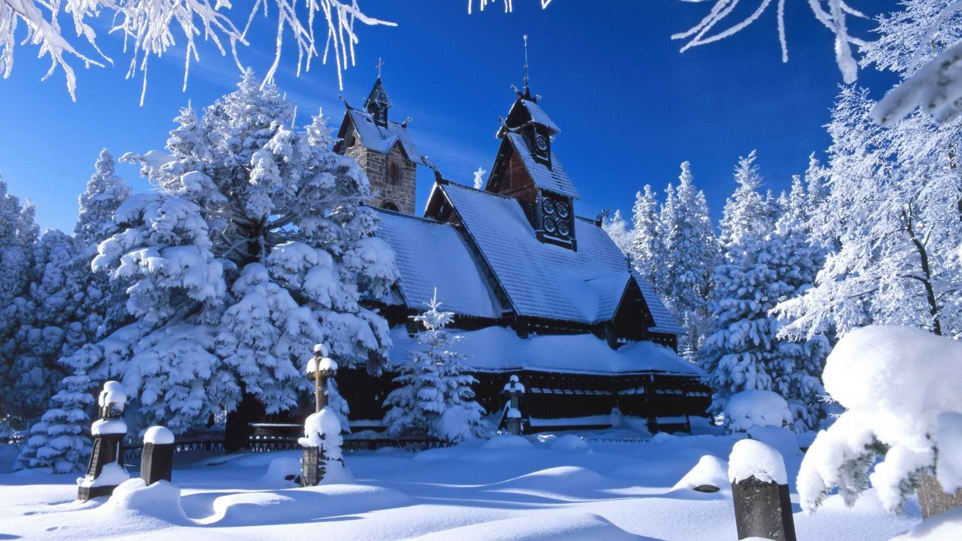 HD desktop wallpaper of a snow-covered church surrounded by frosted trees under a clear blue sky, capturing a serene religious winter scene.