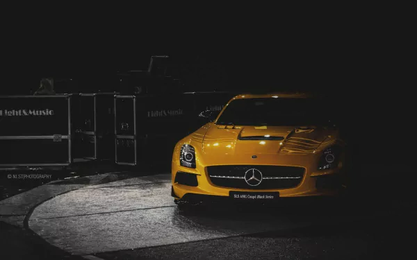 A striking yellow Mercedes-Benz SLS AMG stands illuminated against a dark background, showcasing its sleek design in this HD desktop wallpaper.