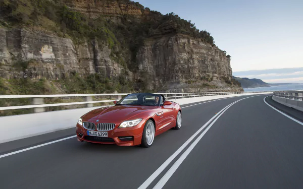 Red BMW Z4 vehicle, a sports convertible, driving along a coastal cliff road — 2K Quad HD PC desktop wallpaper and background.