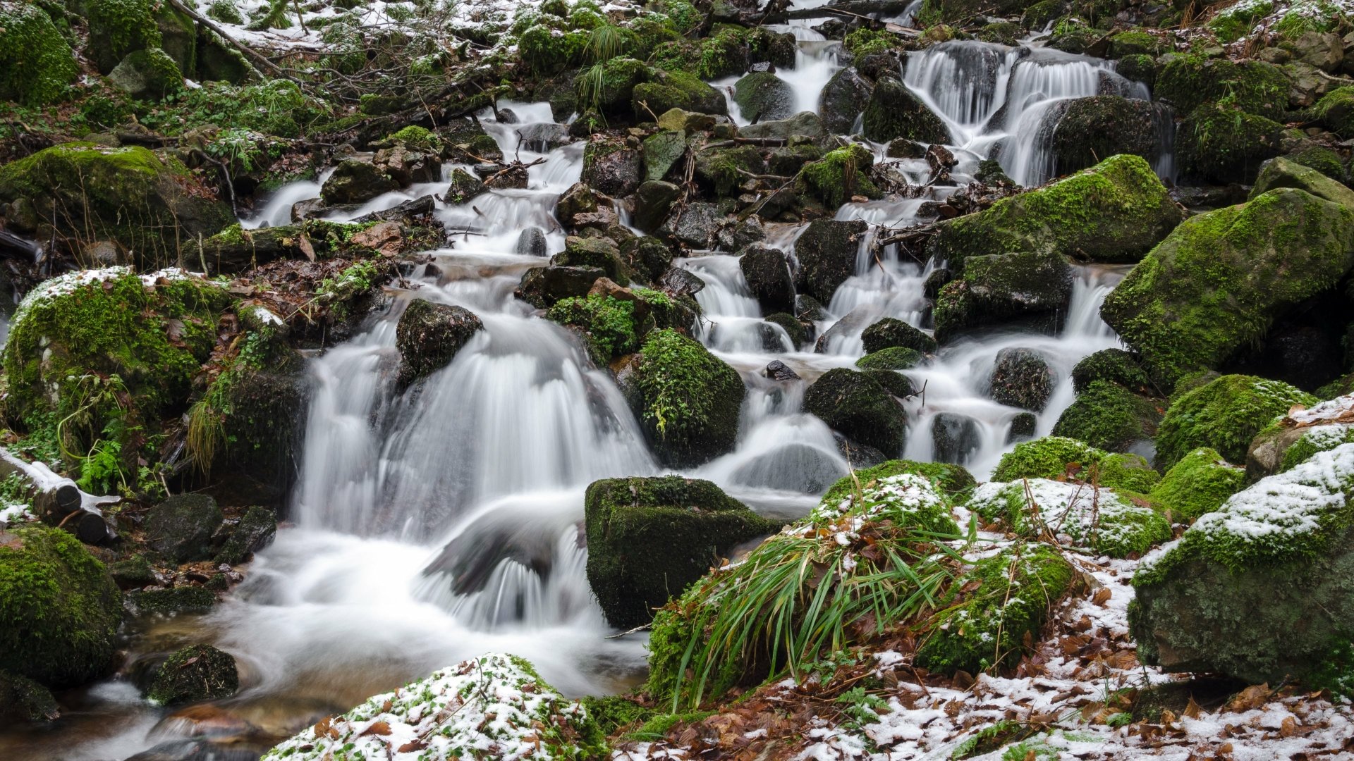 A stunning 4K Ultra HD nature wallpaper featuring a cascading waterfall flowing over moss-covered rocks in a serene forest setting.