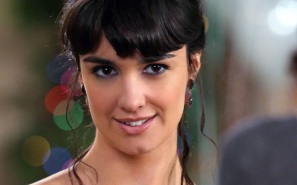 Close-up HD wallpaper of Spanish actress and celebrity Paz Vega with soft background lights, capturing her warm smile and dark hair.