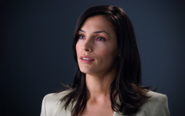 HD desktop wallpaper featuring Dutch actress Famke Janssen with dark hair, wearing a light-colored blazer against a dark background.
