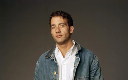 HD PC desktop wallpaper featuring English actor and celebrity Clive Owen against a plain dark background, dressed in a denim jacket over a white shirt.