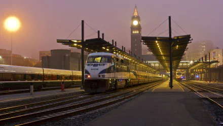 A serene train station at dusk, featuring a train parked under a illuminated canopy, with a clock tower in the background. This image serves as a stunning HD PC desktop wallpaper.