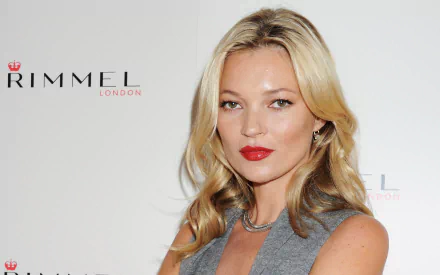 Glamorous studio portrait of a blonde fashion model with red lipstick against a Rimmel backdrop — 2K Quad HD PC desktop wallpaper.