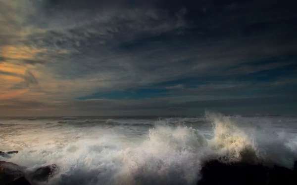 HD nature seascape wallpaper featuring dramatic dark clouds over turbulent ocean waves crashing against rocks at sunset.