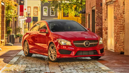 HD PC desktop wallpaper featuring a red Mercedes-Benz CLA-Class parked on a sunlit cobblestone street in an urban setting.