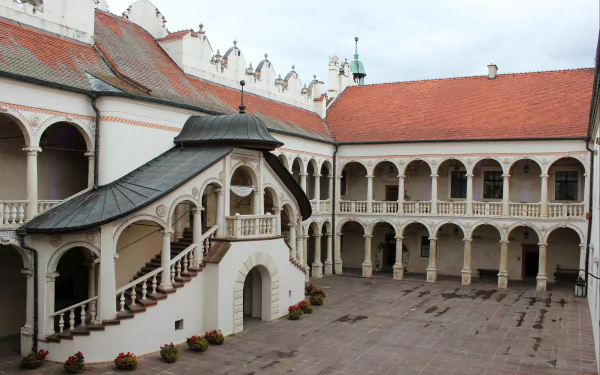 HD desktop wallpaper showcasing the man-made architecture of Baranów Sandomierski Castle courtyard with its ornate balconies and red-tiled roofs under a cloudy sky.