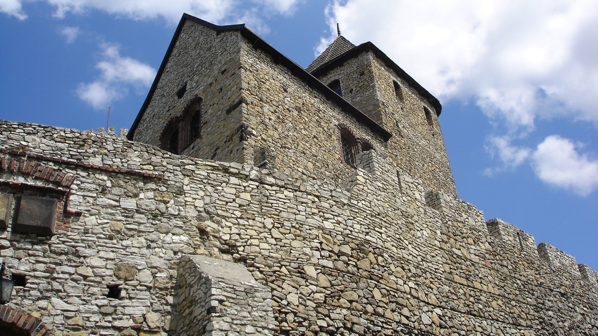 HD PC desktop wallpaper of man-made Bedzin Castle: towering stone walls, arched openings and a crenellated tower beneath a bright blue sky.
