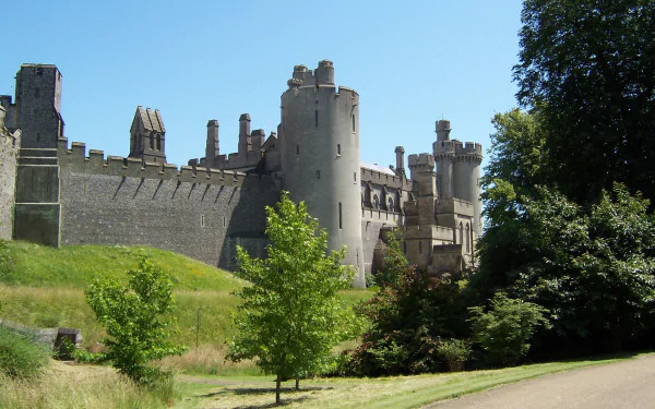 HD PC desktop wallpaper of Arundel Castle — a man-made medieval stone fortress rising above grassy lawns and trees beneath a clear blue sky.