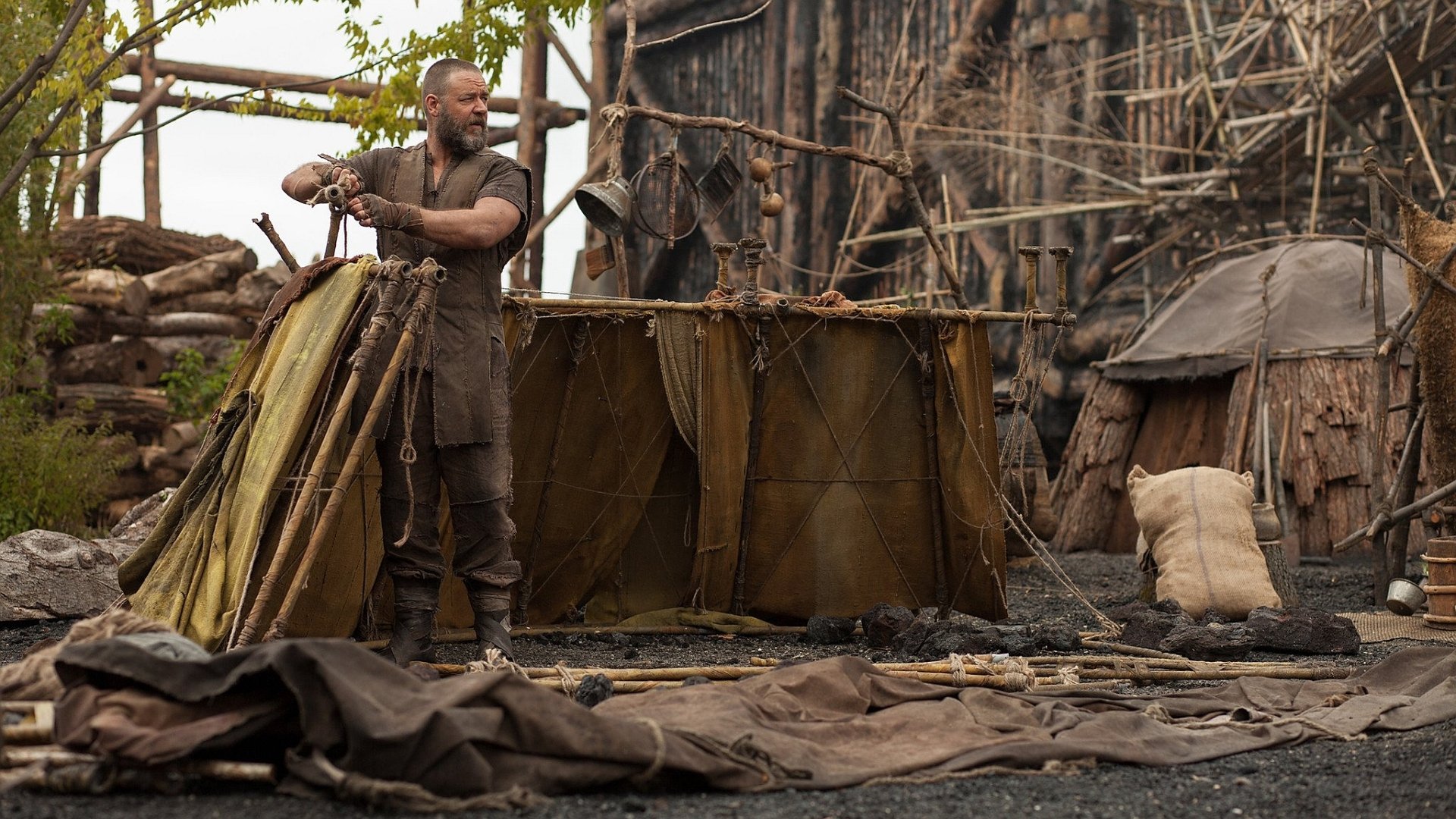 Bearded man in rugged biblical costume assembles a shelter on a shoreline in a scene from the movie Noah — HD PC desktop wallpaper and background.