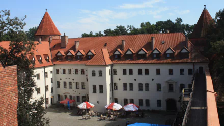 Man-made Bytów Castle courtyard: red-tiled roofs, white façades and plaza umbrellas — HD PC desktop wallpaper background.