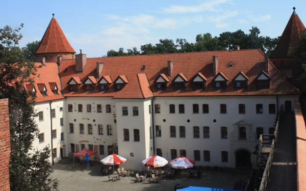Man-made Bytów Castle courtyard: red-tiled roofs, white façades and plaza umbrellas — HD PC desktop wallpaper background.