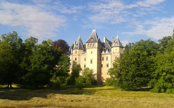 HD desktop wallpaper showing Goluchów Castle, a man-made historic structure surrounded by trees under a partly cloudy sky.