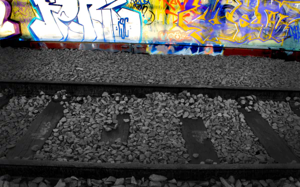 4K Ultra HD PC desktop wallpaper/background of abandoned railroad tracks and gravel leading to a vivid graffiti-covered wall, an artistic urban scene.