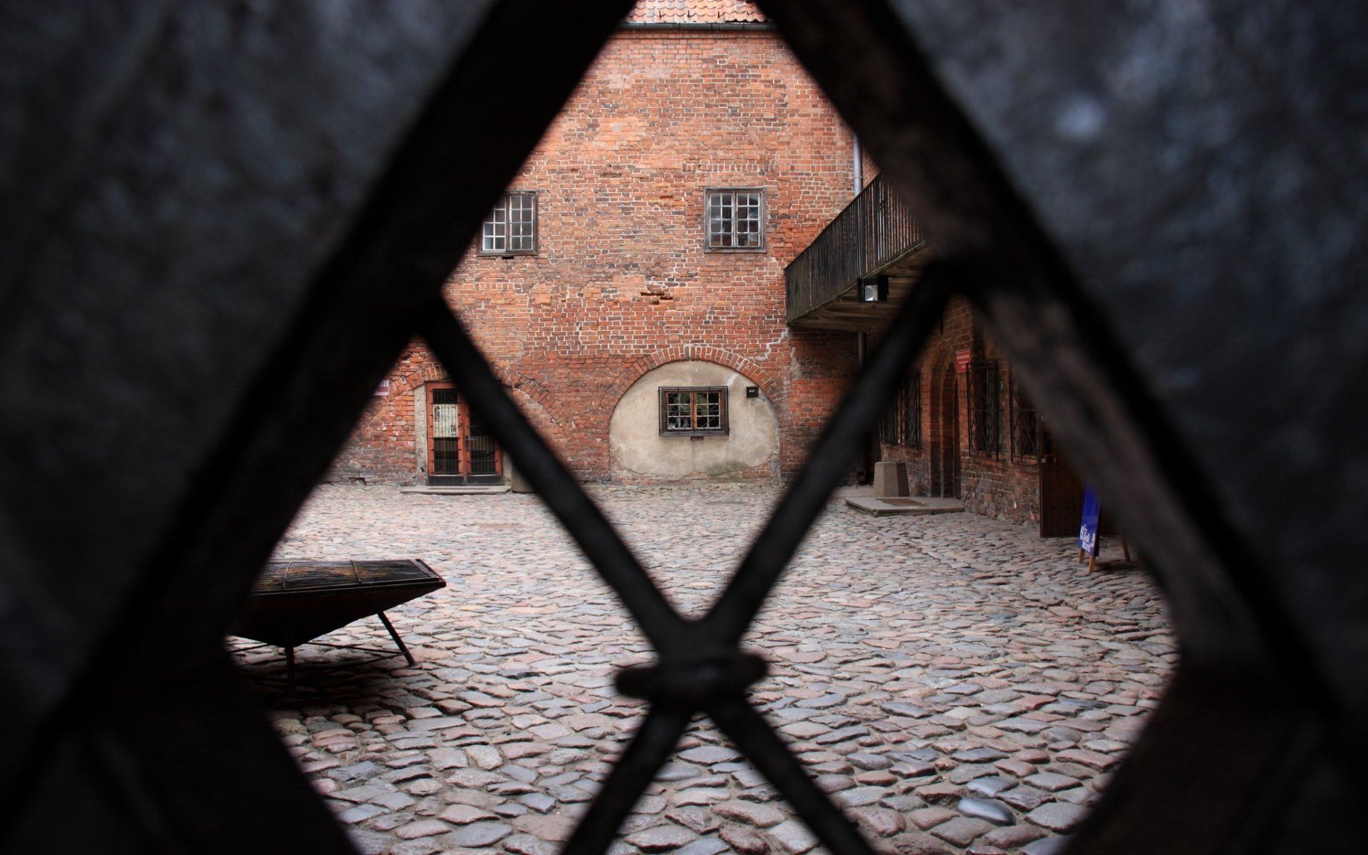 View through a lattice window of the cobblestone courtyard at Kętrzyn Castle, a historic brick architecture in Warmian-Masurian, Poland, Europe.